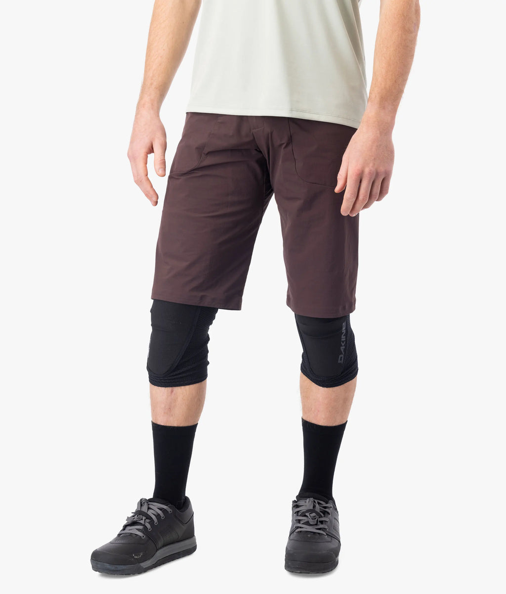 Person wearing brown shorts, black knee pads, and black shoes on a white background