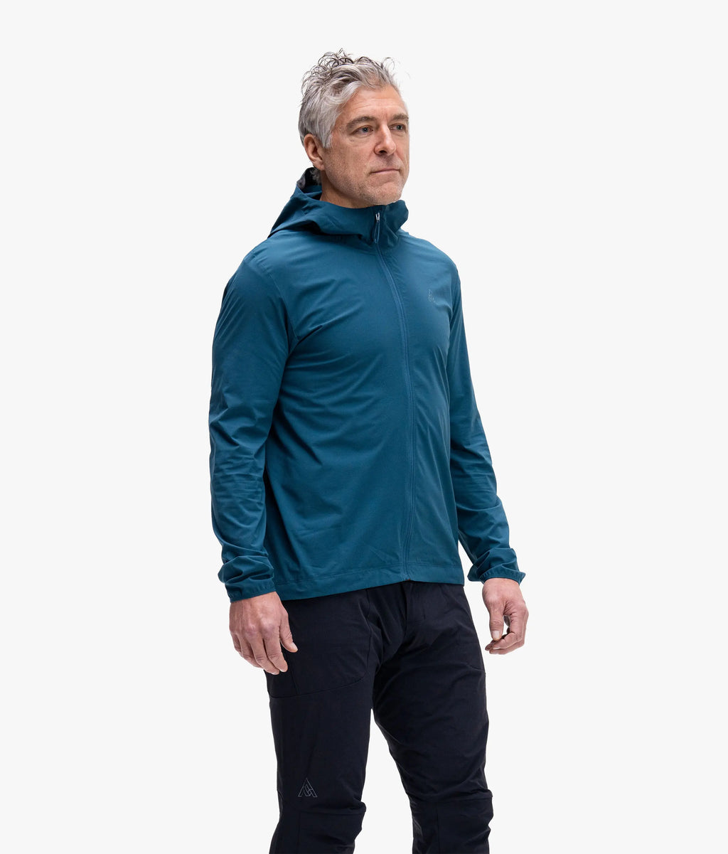 Man wearing a teal jacket and black pants on a white background