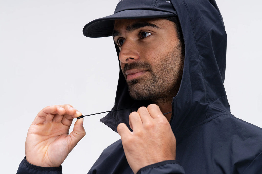 Man wearing a dark raincoat and cap against a light gray background