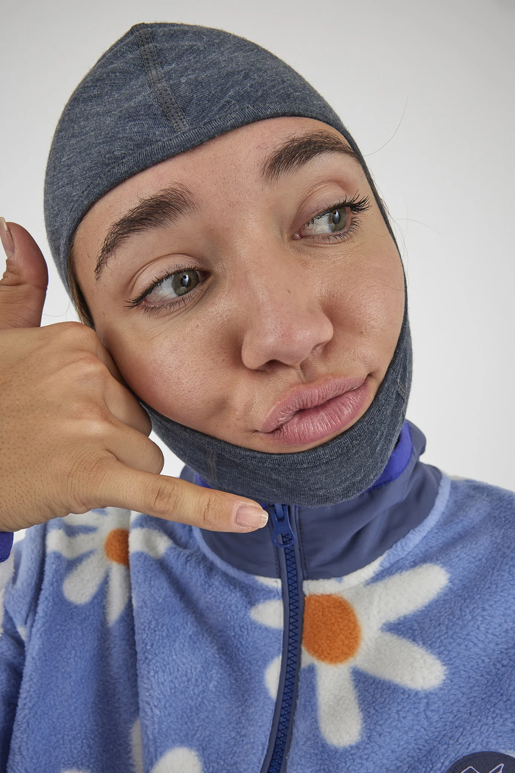Person wearing a blue hoodie with floral patterns and a gray head covering, making a hand gesture.