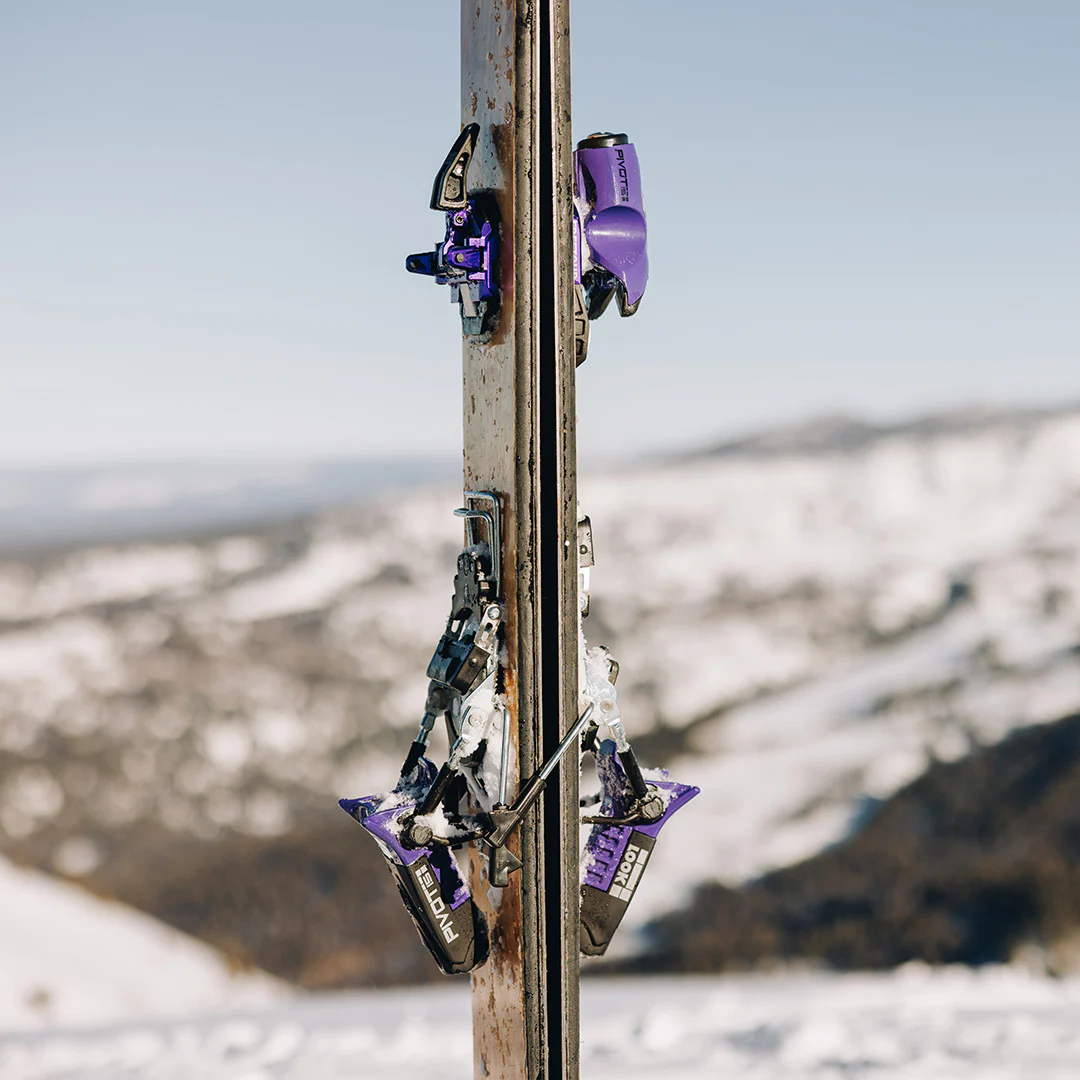 Purple ski bindings attached to a ski with a snowy mountain background