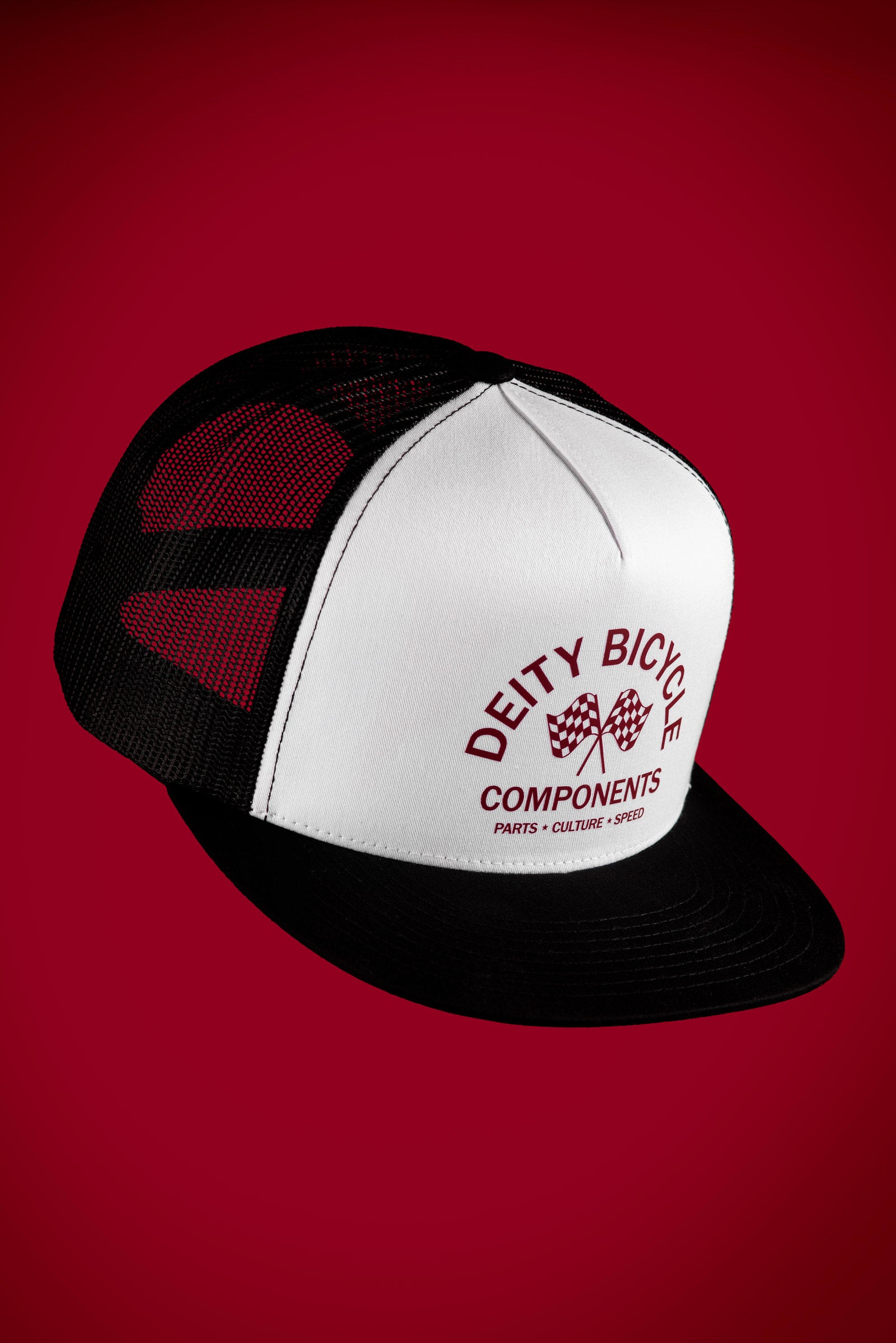 A black and white trucker hat with a white front panel and black mesh back, featuring the 'Deity Bicycle Components' logo in red on the front, set against a solid dark red background.