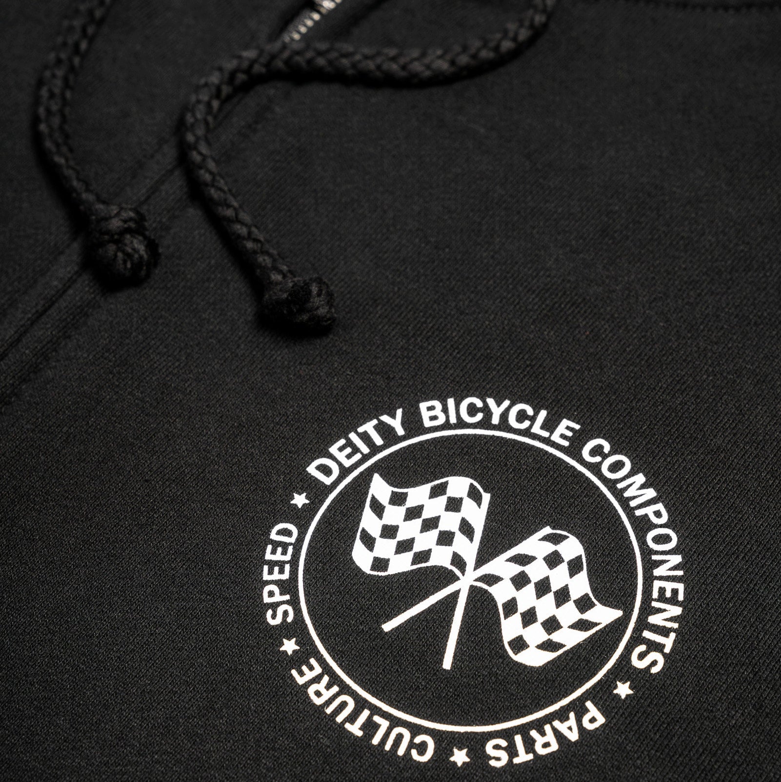 Close-up of a black hoodie with a white circular chest graphic featuring two checkered flags and the text 'DEITY BICYCLE COMPONENTS' and 'SPEED CULTURE PARTS'.