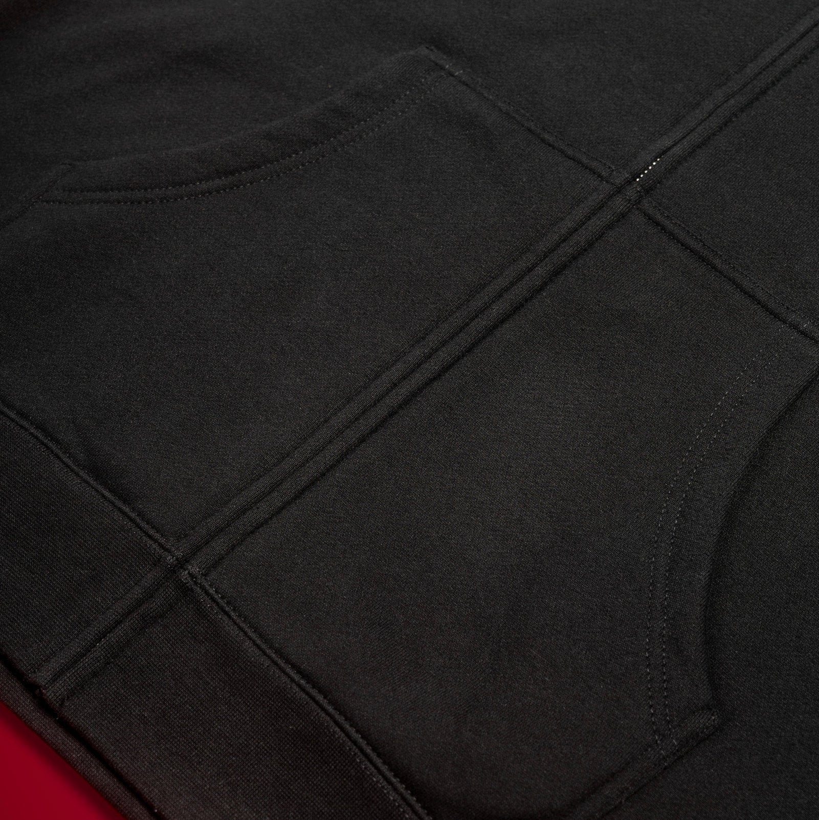 Close-up of a dark charcoal gray garment with visible seam stitching, laid against a red background.