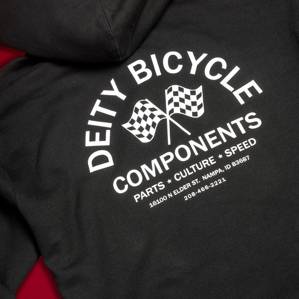 Close-up of a black hoodie showing the back graphic with white text reading 'DEITY BICYCLE COMPONENTS' and two checkered flags, with red fabric visible along the sides.