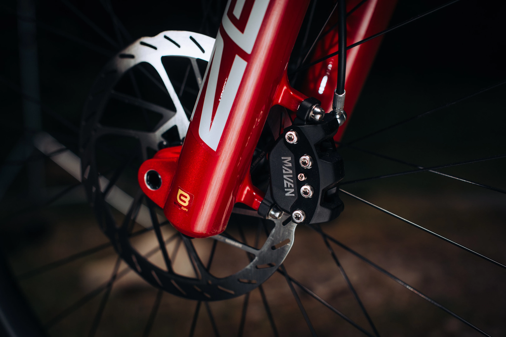 Close-up of a red bicycle fork with a brand logo on a dark background