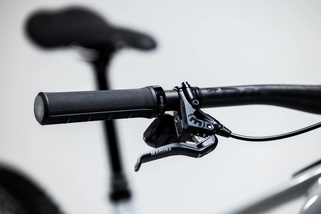 Close-up of a bicycle handlebar with black grips and brake levers on a blurred background
