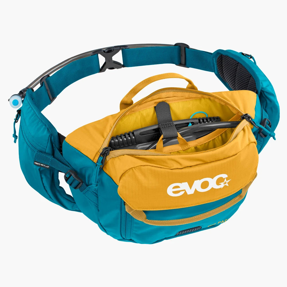 An Evog trail running waist bag in teal and mustard yellow, shown open to display its interior storage capacity and a hydration tube attachment on the side, set against a plain white background.