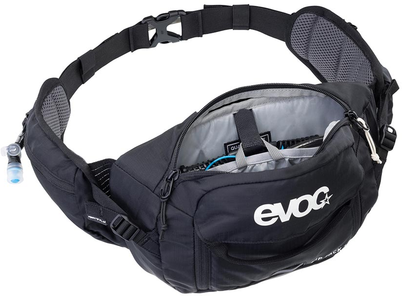 A black Evoc fanny pack with an open front zip pocket showing a gray interior organizer, a side mesh pocket with a blue water bottle, and a white 'evoc' logo on the front, set against a plain white background.