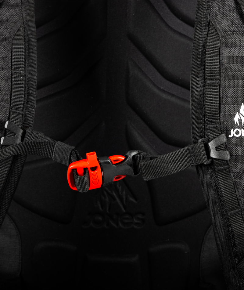 Close-up of a black backpack with a red buckle and visible brand logo.