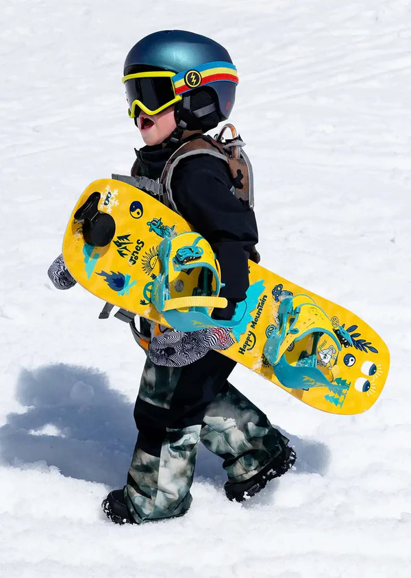 Child holding a yellow snowboard with colorful designs in the snow