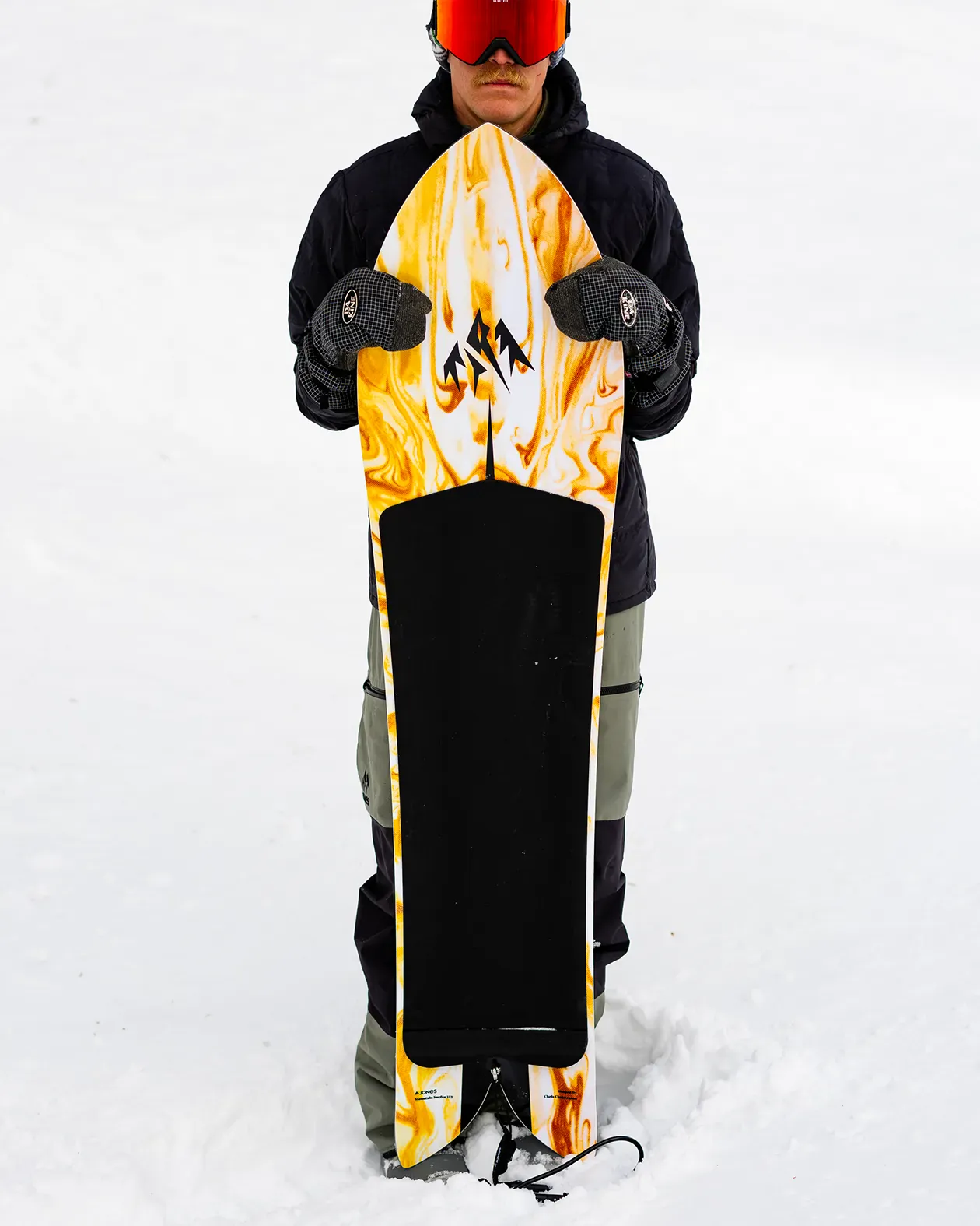 Person holding a snowboard with a flame design in the snow