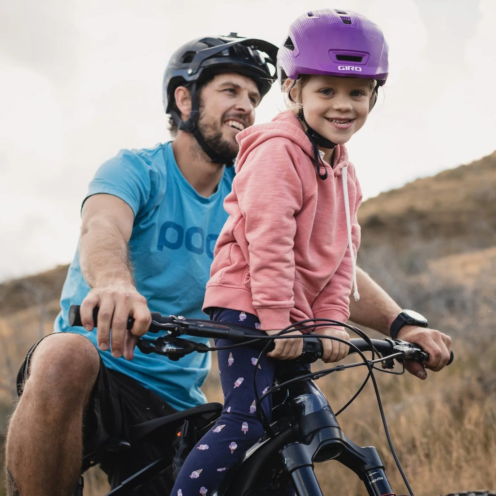 Man and young girl riding a bicycle together with helmets on, outdoors.