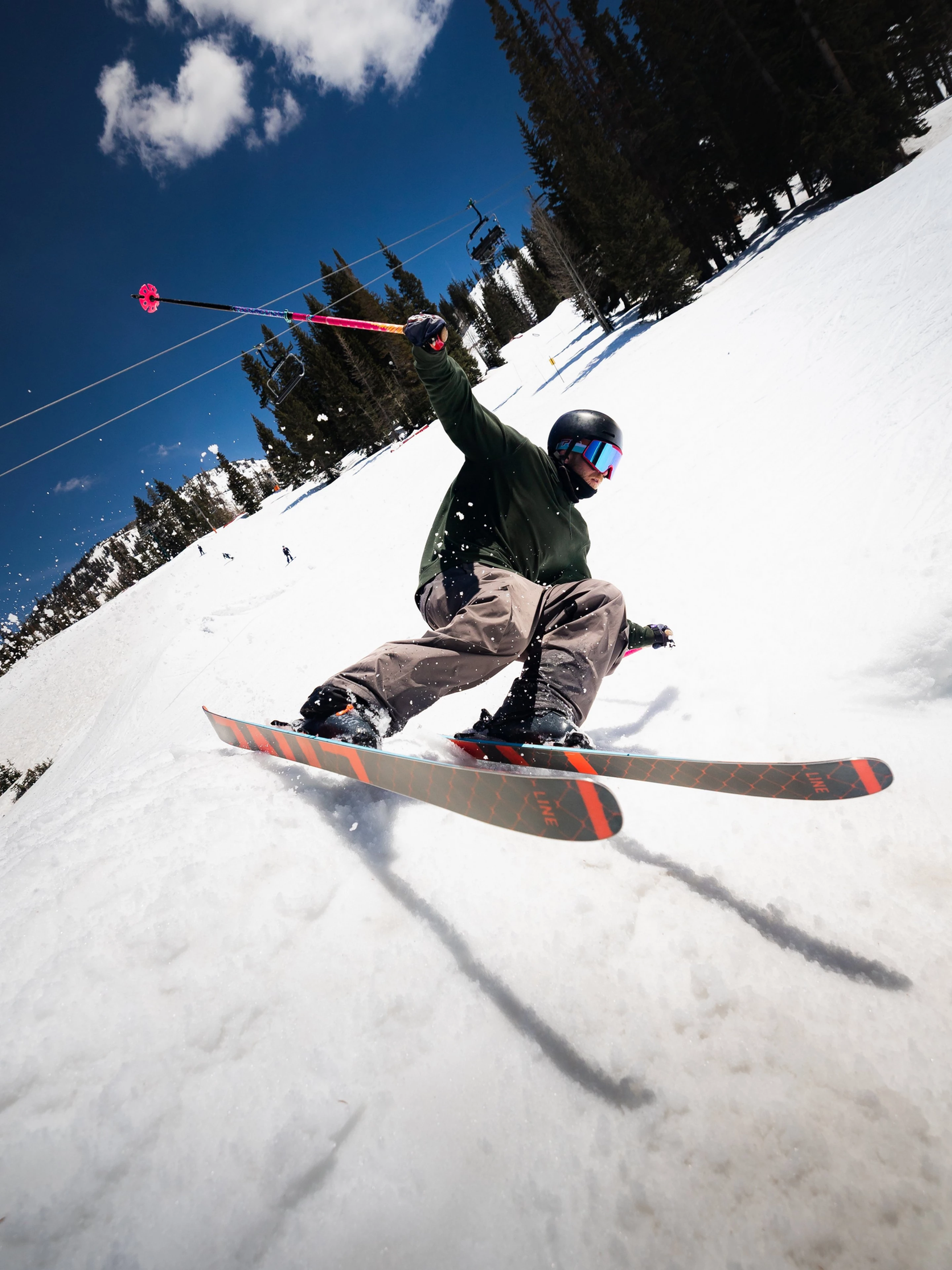 Person skiing down a snowy slope with trees and blue sky in the background