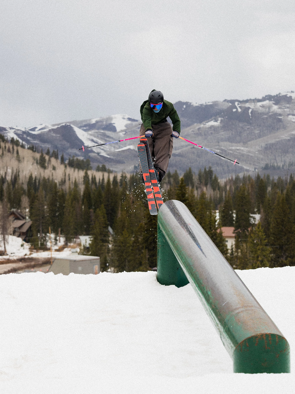 Skier performing a trick on a rail with mountains and trees in the background