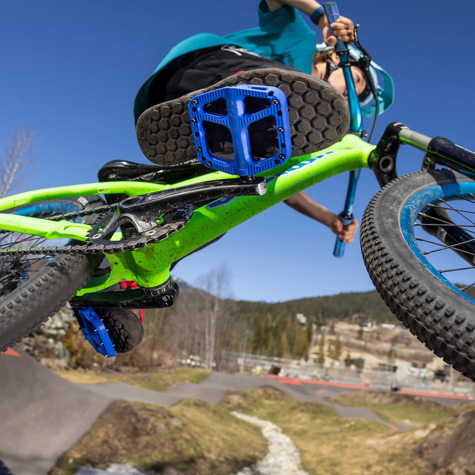 Person performing a bike trick with a green bike against a clear blue sky.