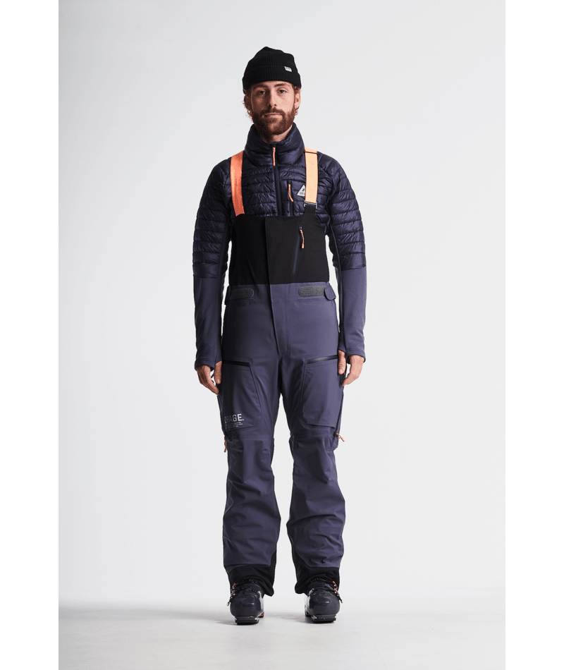 Person wearing a dark blue insulated bib overalls with a black jacket on a white background