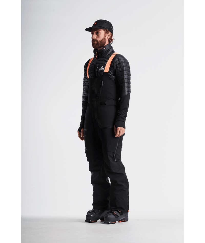 Man wearing a black winter jacket and pants with orange accents on a white background