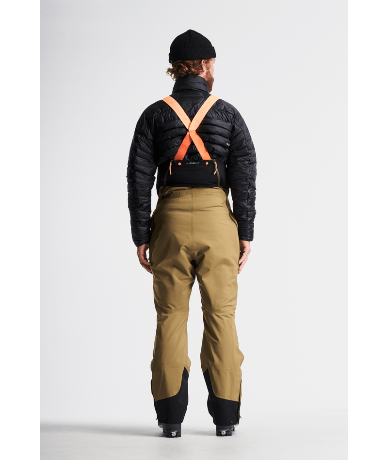 Person wearing a black puffer jacket, beige pants, and orange suspenders on a white background
