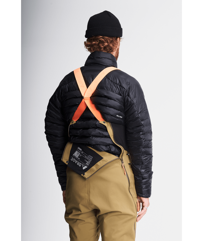 Person wearing a black jacket, beige pants, and a black beanie with an orange harness on a light gray background