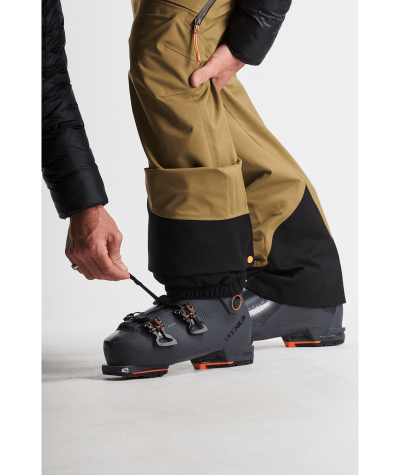 Person wearing brown and black ski pants with a focus on ski boots on a white background