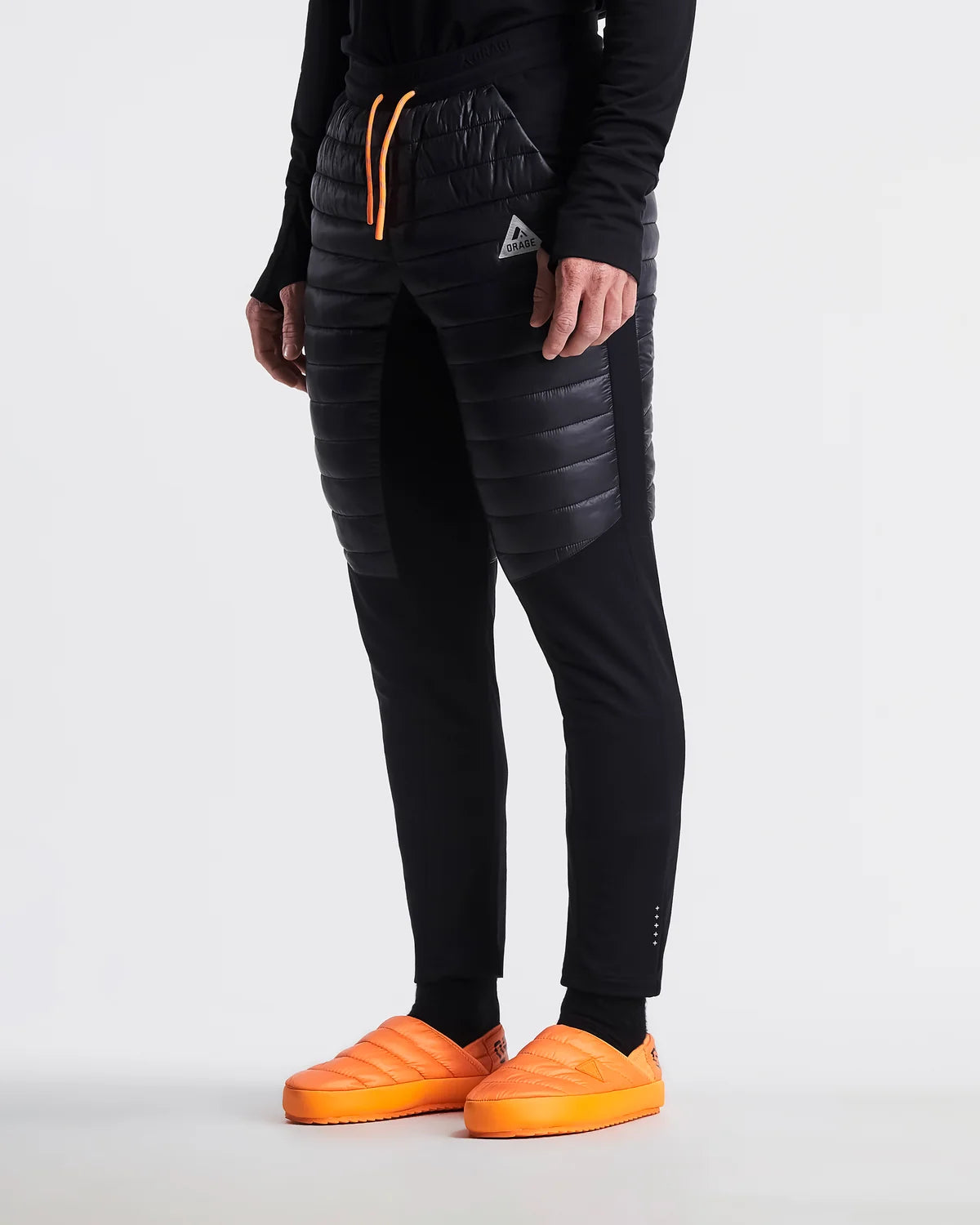 Person wearing black puffer pants with orange accents and orange shoes on a white background