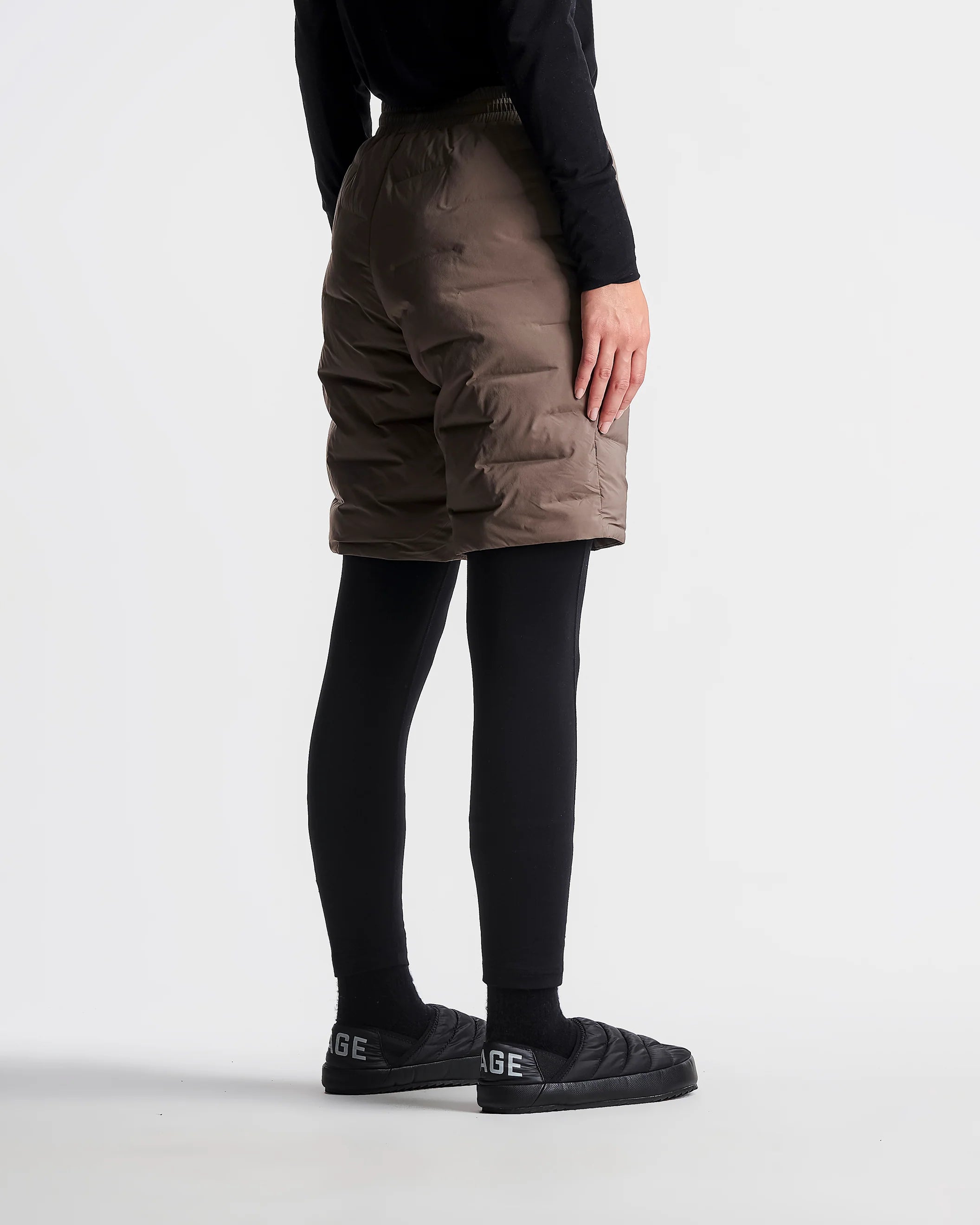 Person wearing brown cargo shorts and black shoes on a white background