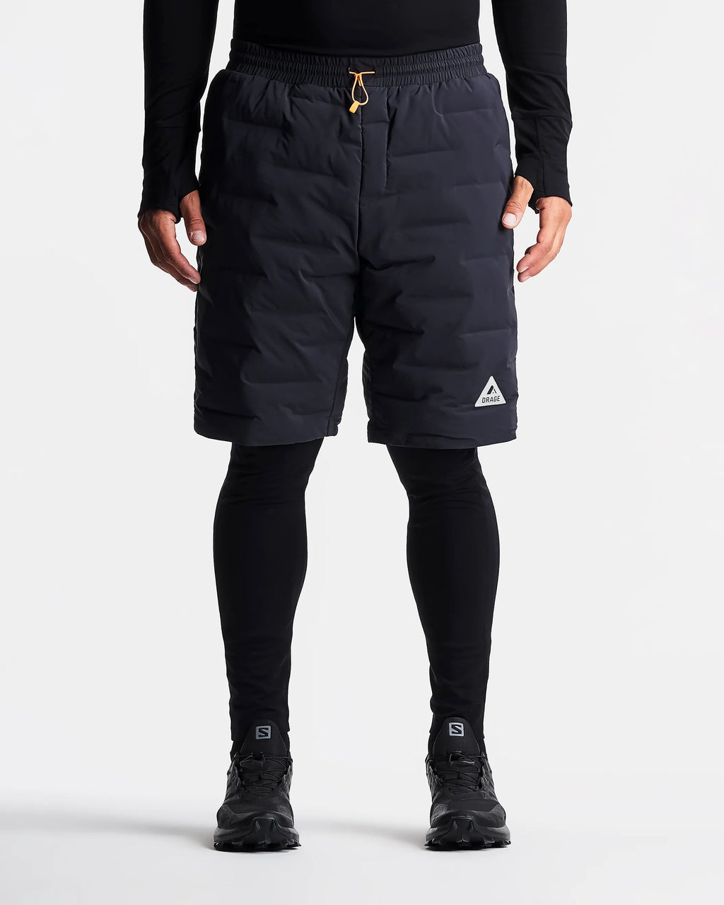 Person wearing black shorts with a brand logo on a white background