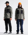 Two people wearing matching gray jackets with black patches on a white background