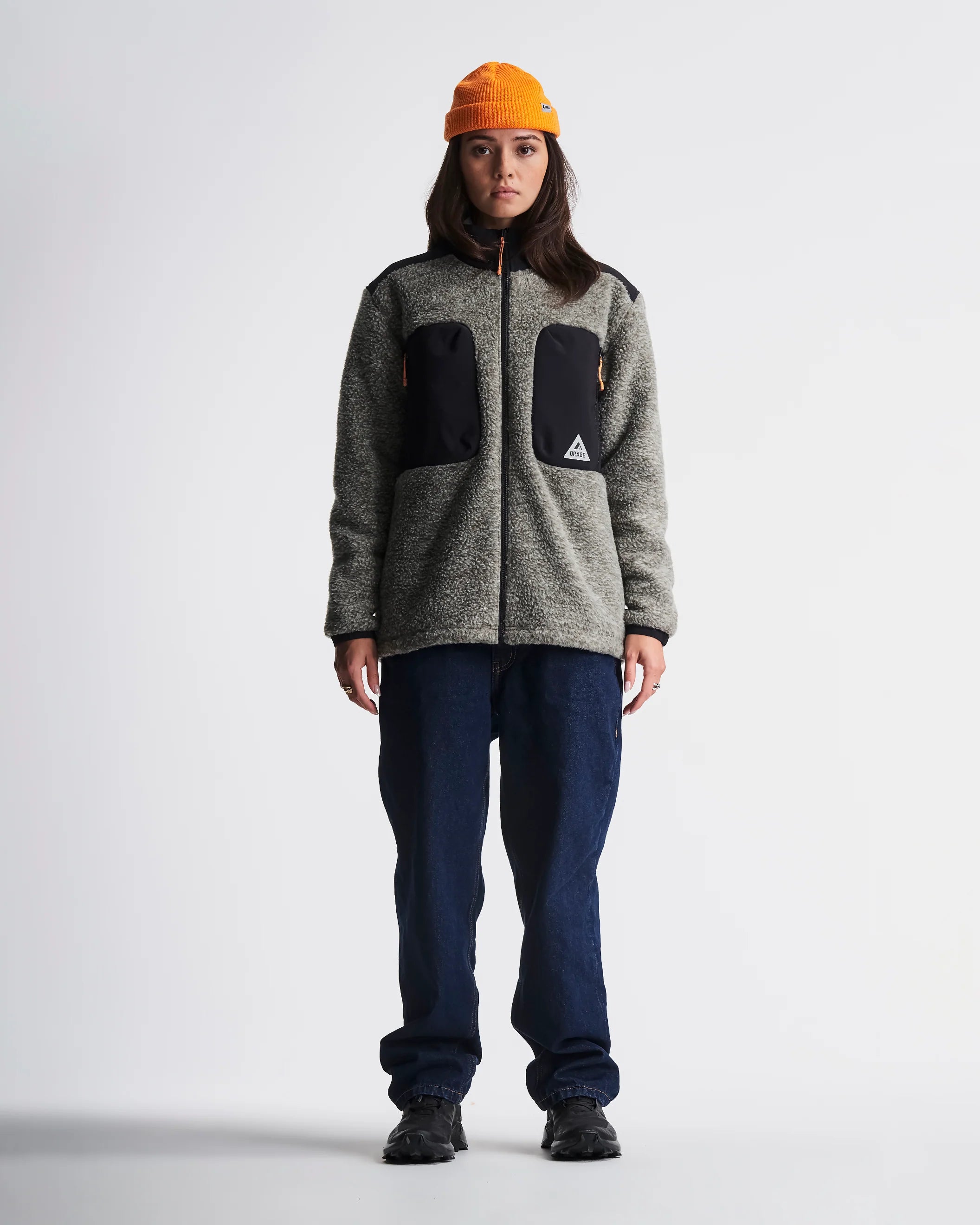 Person wearing a gray jacket with black patches and an orange beanie on a white background