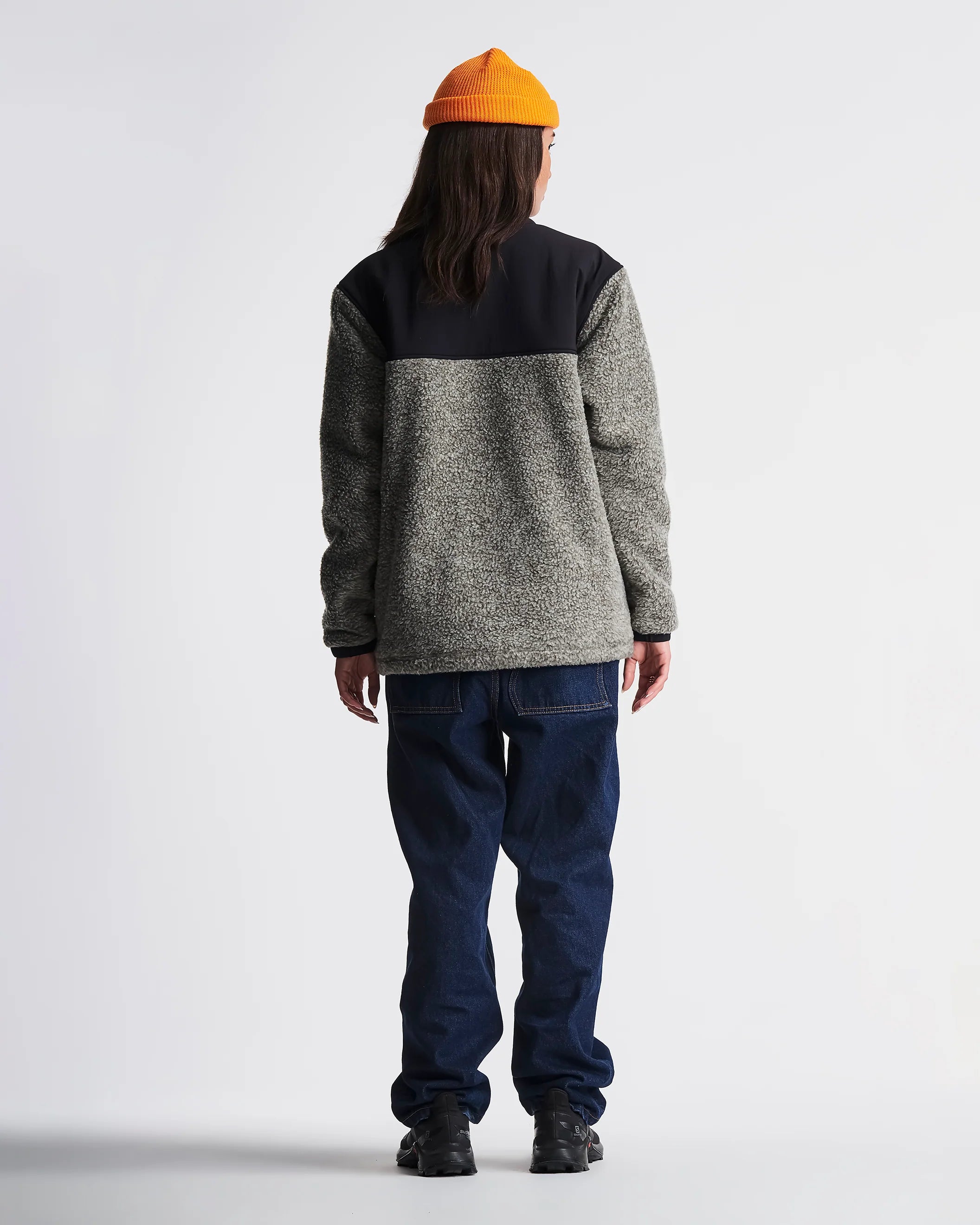 Person wearing a gray and black color-blocked sweater with blue pants on a white background