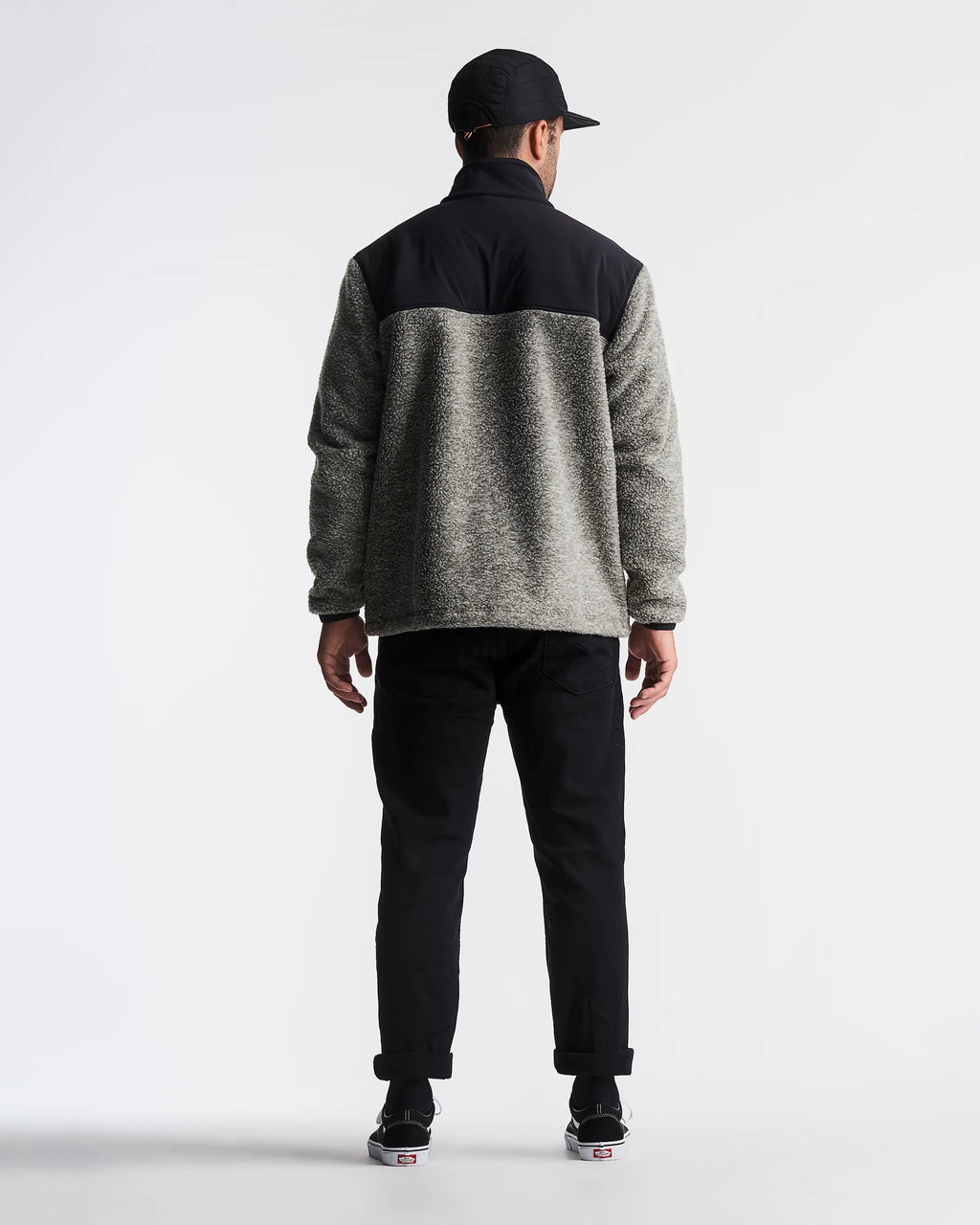 Person wearing a gray and black pullover with black pants on a white background