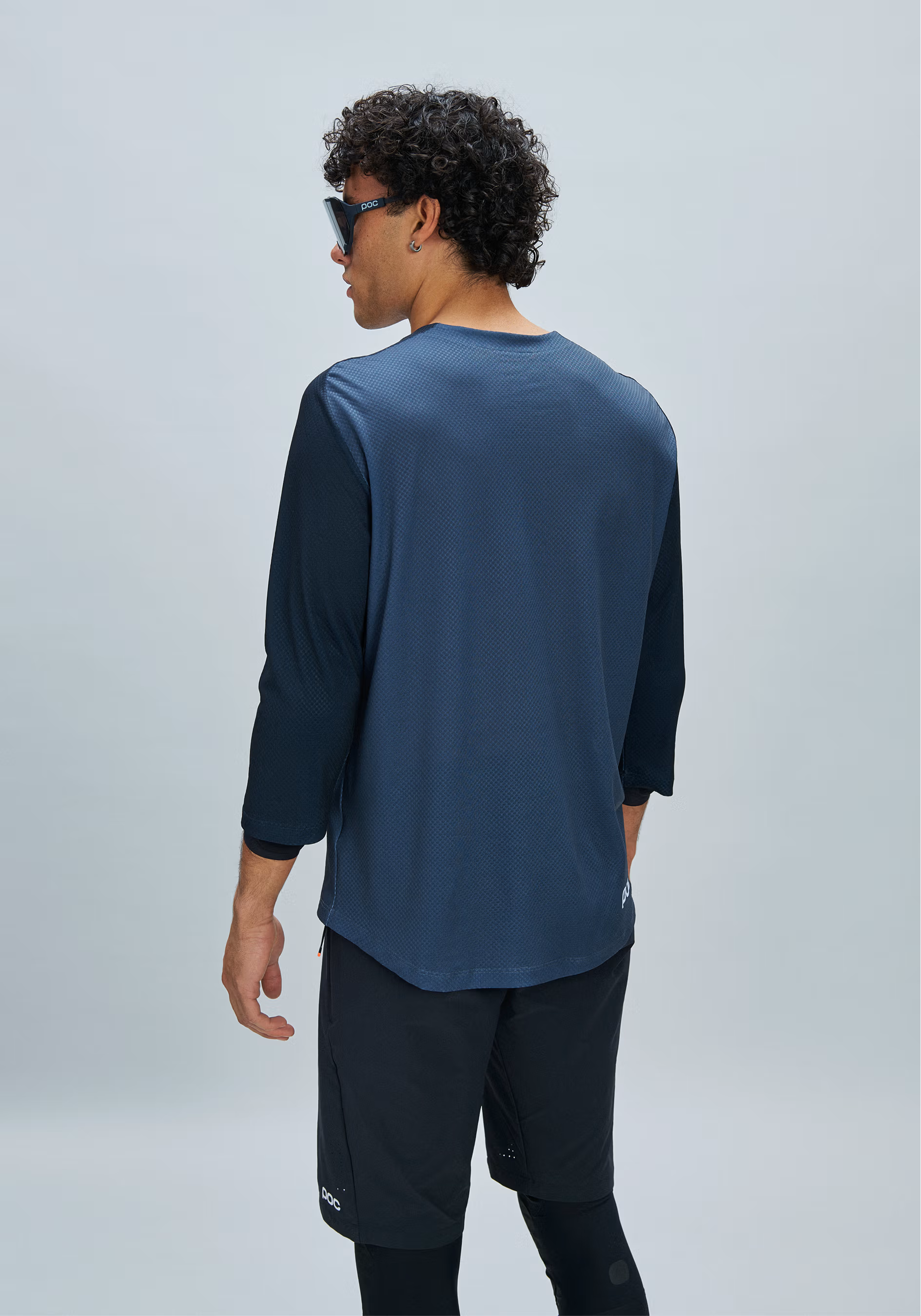 A man wearing a navy blue long-sleeve athletic shirt and black athletic shorts, photographed from the back against a light gray studio background.