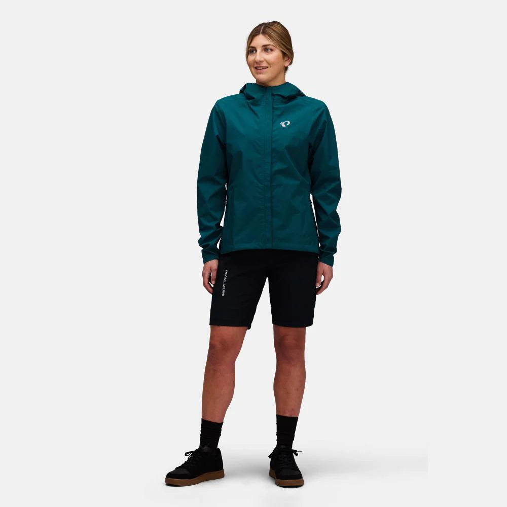 A woman modeling a dark teal hooded athletic jacket and black athletic shorts against a light gray studio background.