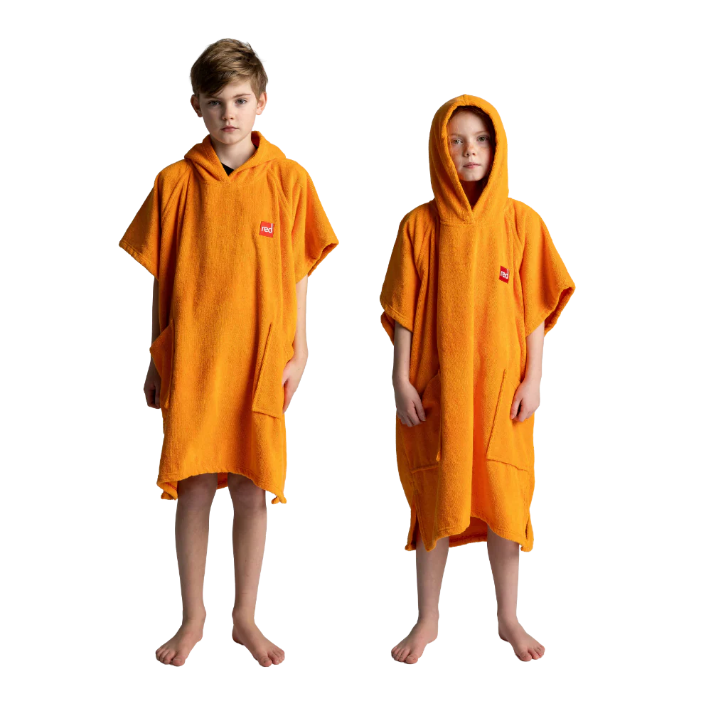 Two children standing barefoot against a white background, each wearing a bright orange hooded towel poncho with short sleeves and front pockets. A small red square logo patch is visible on the chest of each poncho.