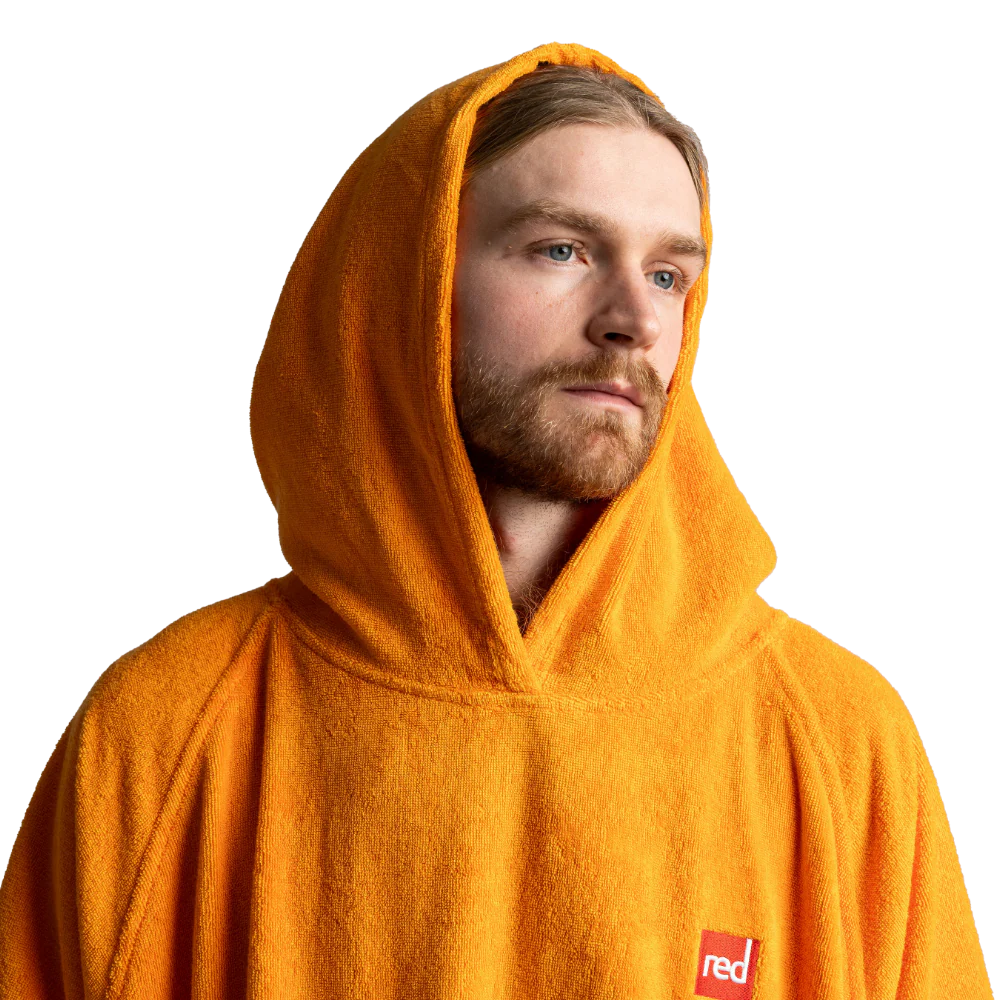 A man wearing a bright orange hooded towel hoodie, shown from the chest up against a plain white background. A small red square logo with white text is visible on the lower right chest area.
