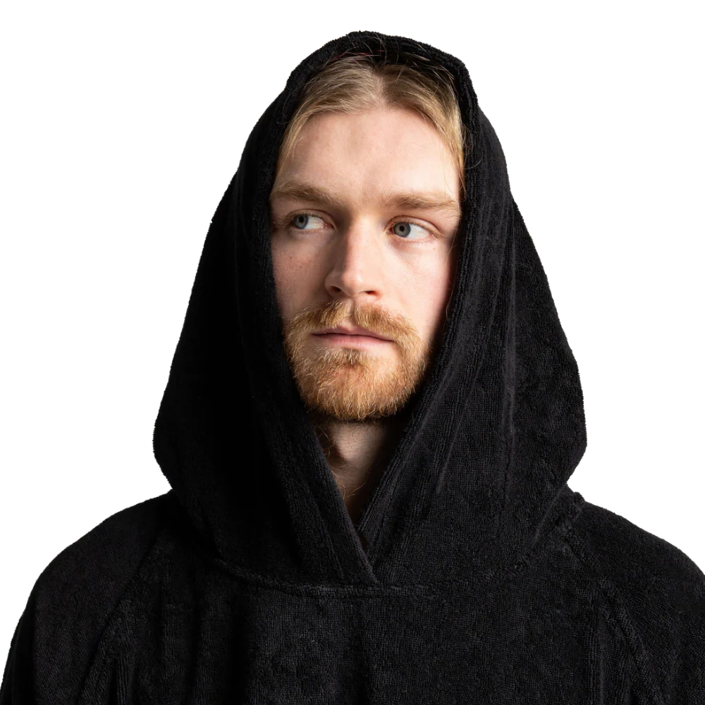 A man wearing a black hooded robe or poncho, shown from the chest up against a plain white background.