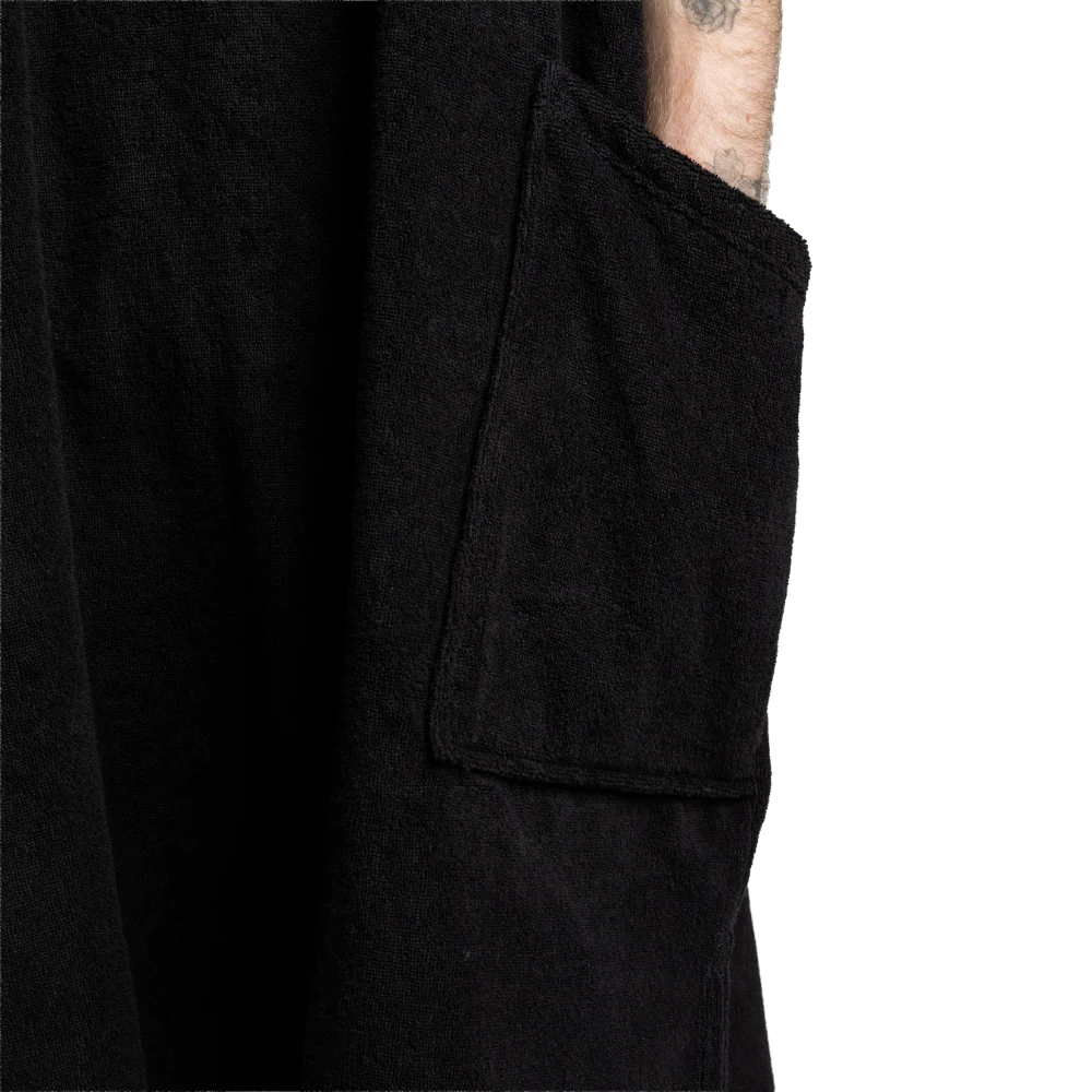 Close-up of a black textured garment with a large patch pocket and a tattooed arm visible at the cuff, against a plain white background.