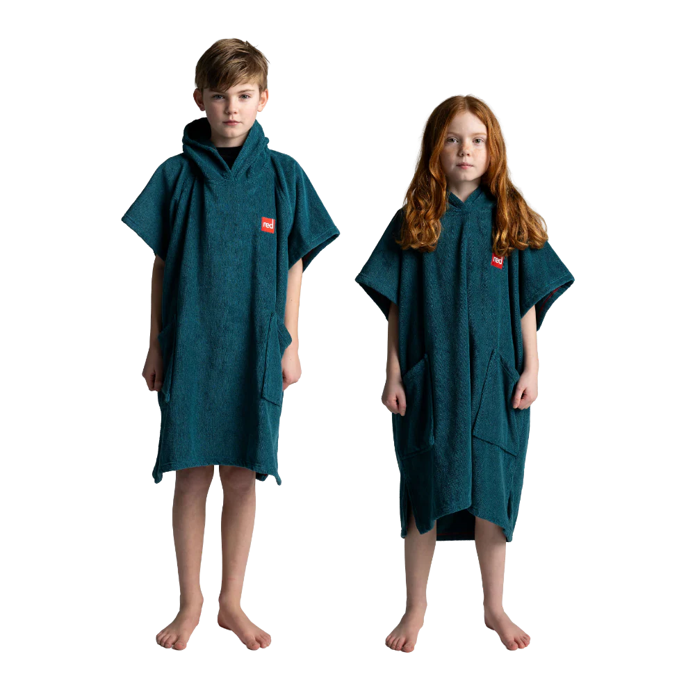 A boy and a girl standing barefoot against a white background, each wearing a dark teal hooded towel poncho with a small red square logo on the chest.
