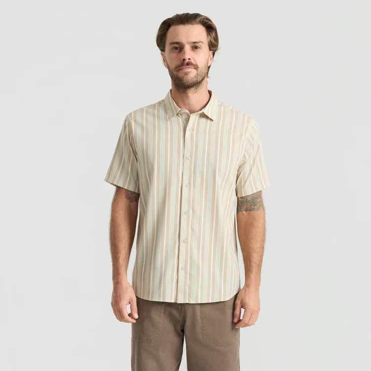 Man wearing a striped shirt and brown pants on a light gray background
