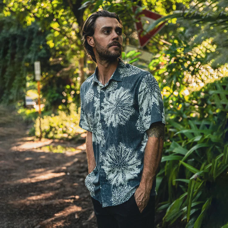 Man wearing a blue floral shirt standing in a forested area