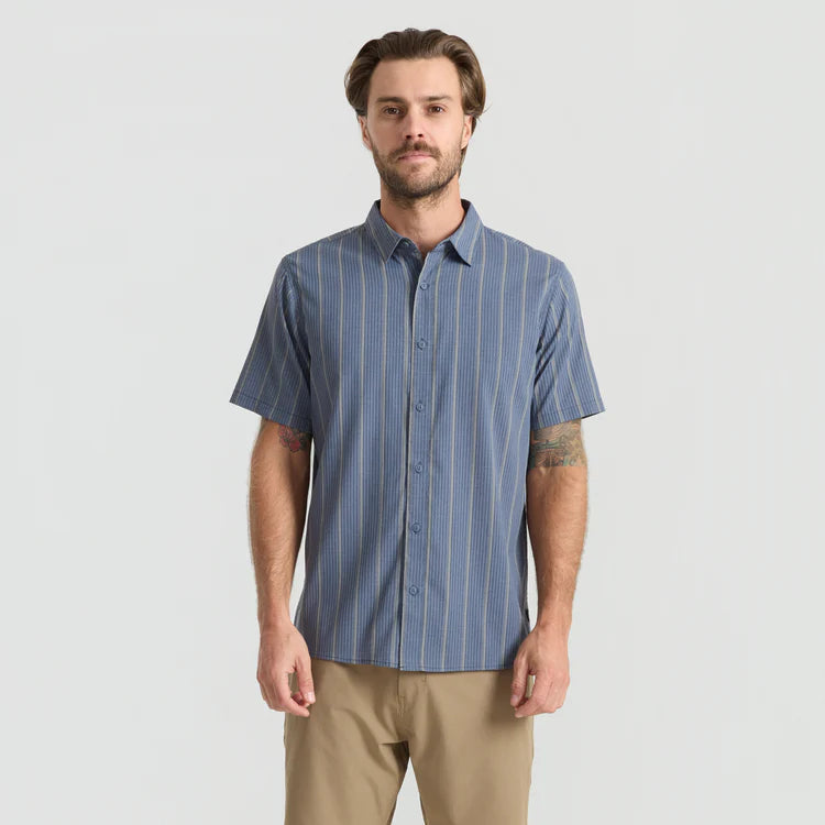 Man wearing a blue striped shirt and beige pants on a light gray background