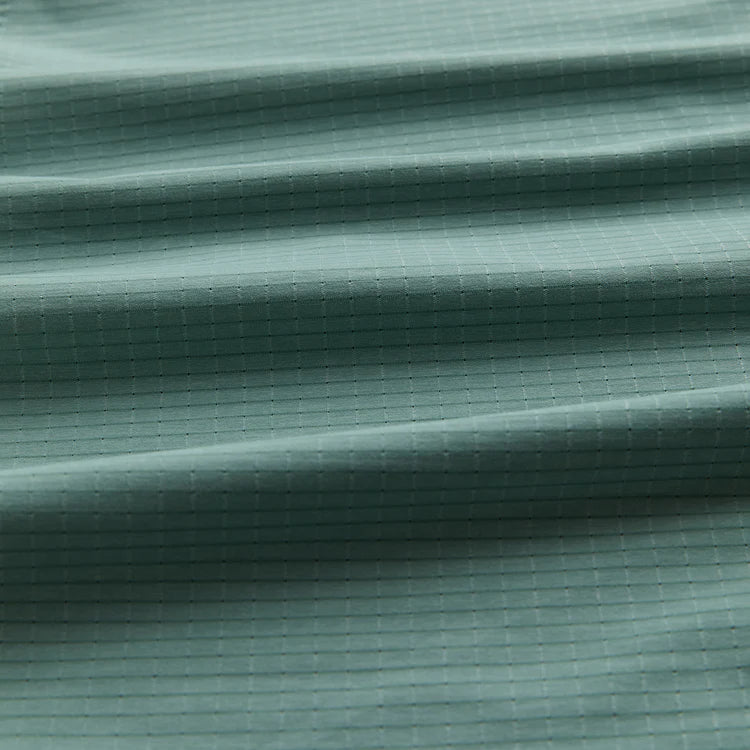 A close-up of a textured fabric with a fine grid pattern in a muted sage green color, showing soft horizontal folds.