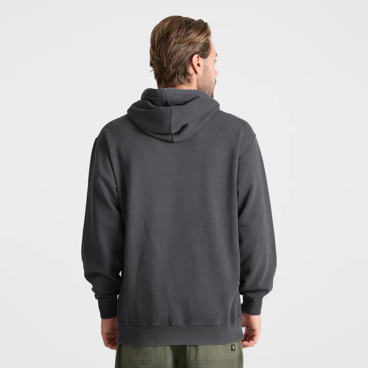 A man viewed from the back wearing a dark charcoal gray pullover hoodie, paired with olive green pants, against a plain light gray studio background.