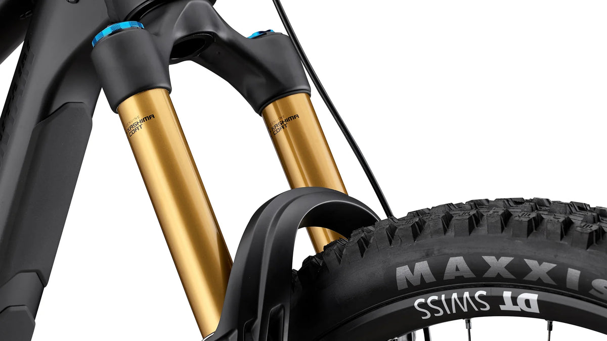 Close-up of a mountain bike suspension fork with gold and black components, paired with a knobby Maxxis tire on a white background.