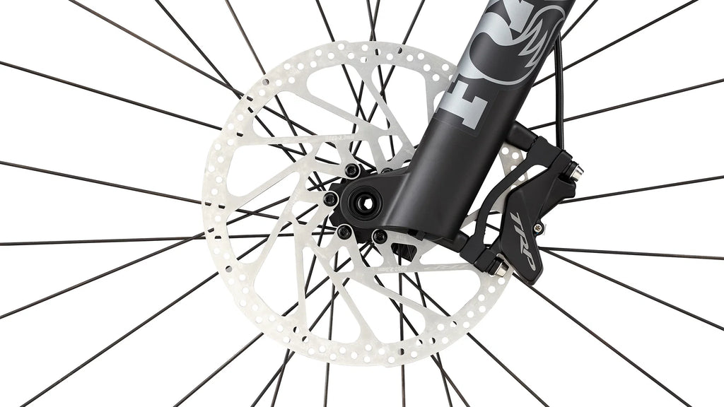Close-up of a bicycle front wheel showing a black disc brake rotor, silver spokes, and a black fork with a visible Fox logo.