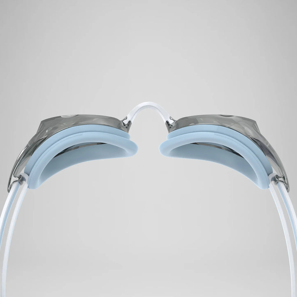 Close-up rear view of swimming goggles showing the white straps, light blue silicone pads, and metallic silver frame against a neutral gray background.