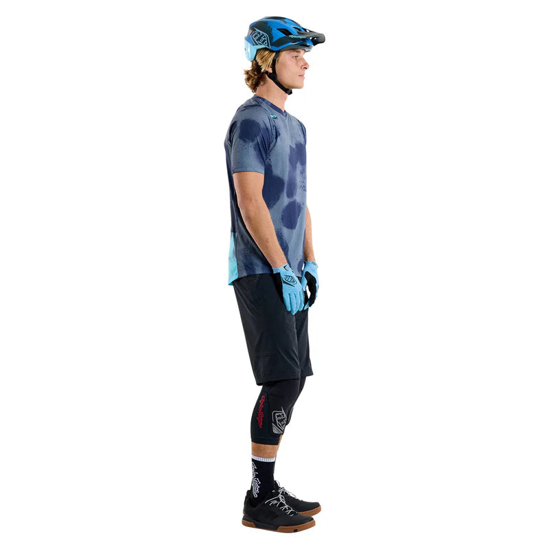 Person wearing a blue and black tie-dye shirt, black shorts, and protective gear on a white background
