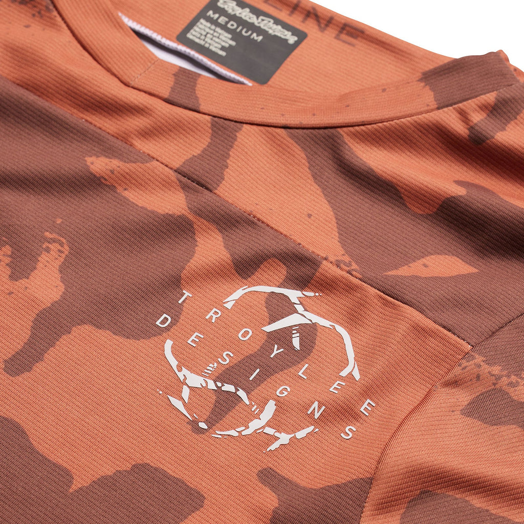 Camouflage-patterned shirt with a logo and text on a brown background