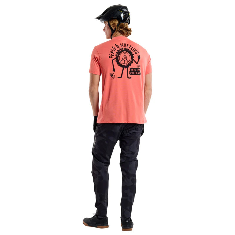 Person wearing a coral t-shirt with a graphic design on the back, standing against a white background.